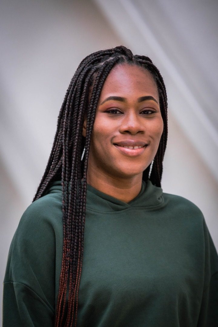 Dorcas B., wearing long knotless braids and a forest green sweatshirt